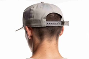 Homme portant une casquette snapback à visière plate dans un style streetwear épuré. Gros plan sur le mécanisme d'ajustement à pression à l'arrière, fond blanc studio